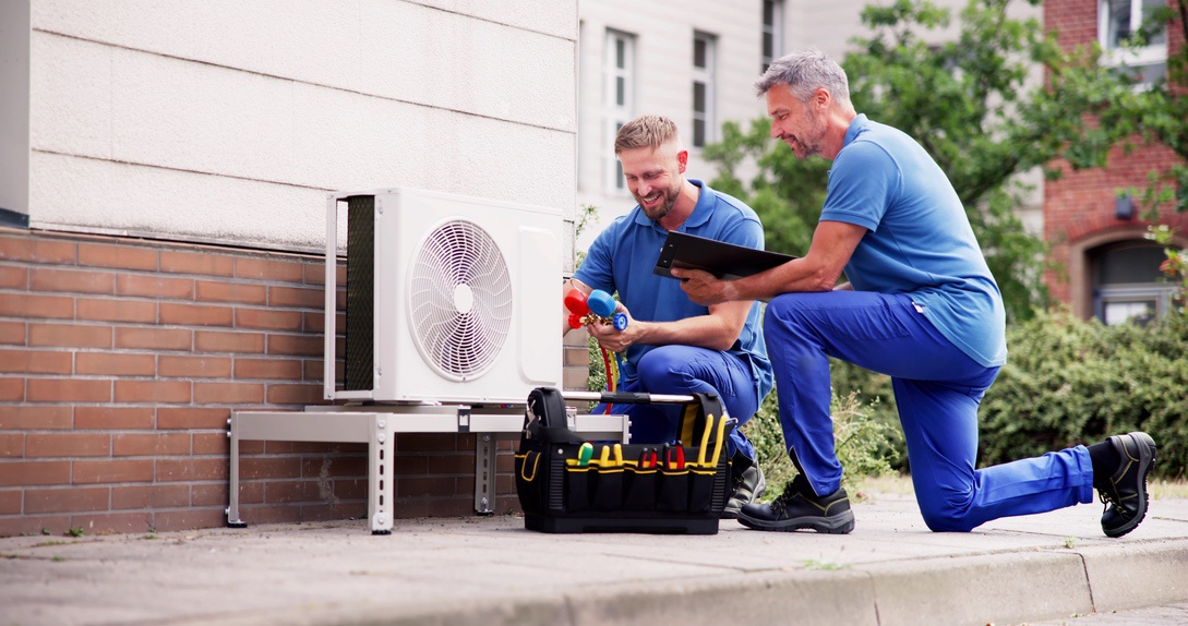 Two men providing maintenance to a heat pump outside